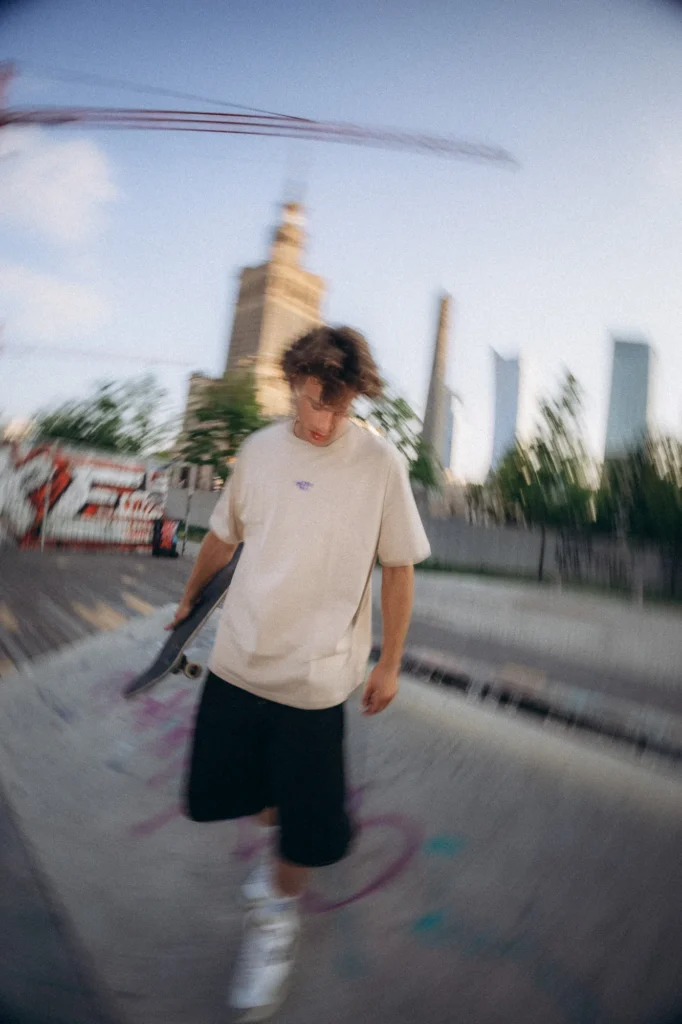 Skater w koszulce Miejska Fala jedzie na deskorolce, w tle Pałac Kultury