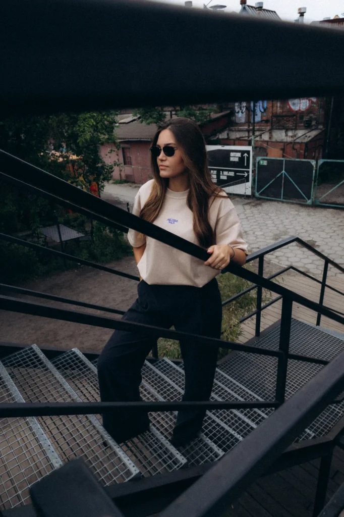 Kobieta w koszulce Miejska Fala schodzi metalowymi schodami