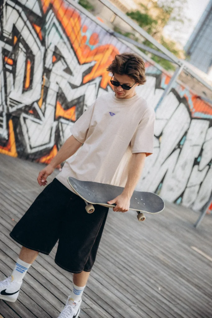 Skater w koszulce Miejska Fala trzyma deskorolkę przy ścianie z graffiti