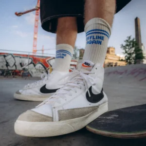 Białe skarpety Offline Again z niebieskimi paskami i napisem, noszone do sneakersów na skateparku
